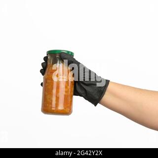 Female hand in a black glove holds a glass jar with cooked beans in tomato sauce Stock Photo