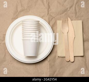 Disposable round white paper plates and cups on brown paper background, top view Stock Photo
