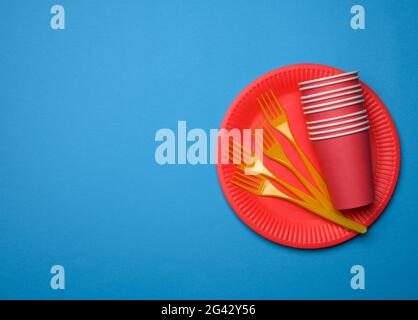 Orange plastic forks and empty red paper disposable plates on a blue background Stock Photo
