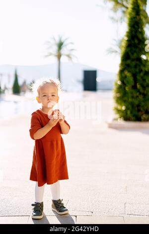 An adorable 2-year old is eating a sweet roll in the park by the sea Stock Photo