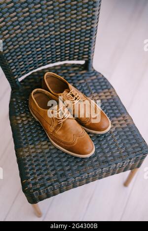 Mens brown stylish shoes with laces on a gray wicker chair.