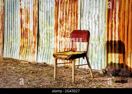 Old wooden chair in front of rusted metal wall, California, USA Stock Photo