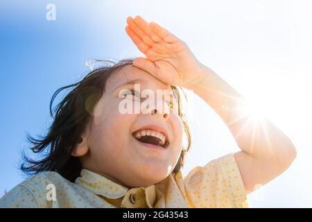 Happy smiling boy in flare sunshine with  hand at forehead Stock Photo