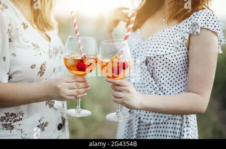 Two young women carrying goblet of alcohol cocktail with cherries and striped straw Stock Photo