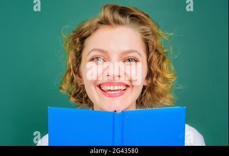 Smiling teacher in classroom. Female lecturer with book. School subjects. Education. Stock Photo