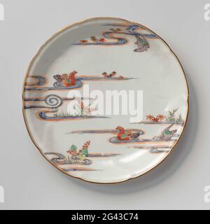 Saucer-dish with Flower Sprays in Relief and Two Mandarin Ducks in a pound. Scale of porcelain with a scalloped edge, painted on the glaze in blue, red, green, yellow, eggplant, black and gold. On the front on the wall flower branches in relief; Two mandarin people in a pond with plants and a flying bird in an email colors. The outside with flowering aquatic plants. Five preen on the bottom. Kakiemon style. Stock Photo