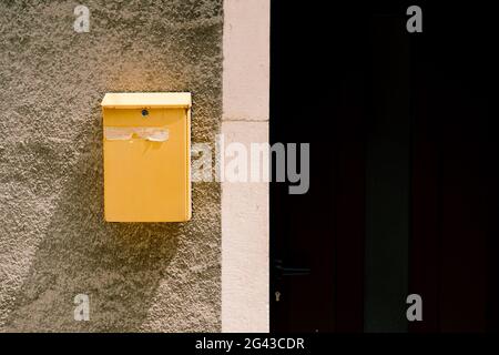 A yellow mailbox on a sunny day on a stone wall near the door to the house.