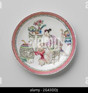 Saucer with a Chinese Lady, Boy and Rabbit. Dish of porcelain, painted on the glaze in blue, red, pink, green, yellow, purple, black and gold. On the flat of the dish a Chinese lady on a chair with a boy next to her with a rabbit for him; They are surrounded by lucky objects such as a dragon vase, vase with coral and peacock feathers, flower vase, fruit basket, incense burner and a vase with rolls; The inner edge with a decorative bond with napkin. Dish has been broken. Family Rose. Stock Photo