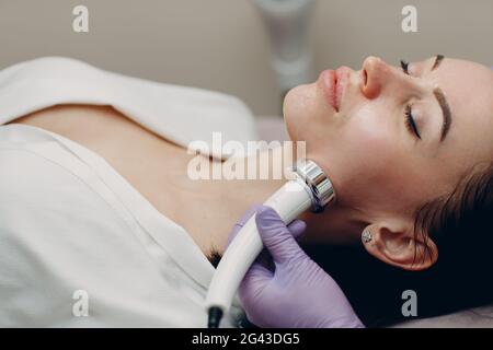 Young woman receiving electric RF lifting facial massage at beauty spa with electroporation equipment. Stock Photo