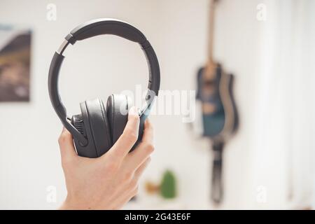Enjoying music at home: Young Caucasian man is black holding wireless headphones Stock Photo