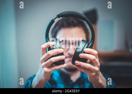 Enjoying music at home: Young Caucasian man is black holding wireless headphones Stock Photo
