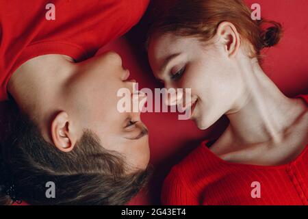 Two young people enjoying on the floor. Couple lovers man and woman lies on red background. Stock Photo