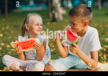 To cute kids lttle boy and girl eating juicy watermelon in the picnic at autumn park meadow Stock Photo