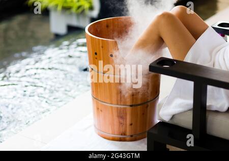 A woman having a footbath, in wooden barrel , with steam billowing. Horizontal. Kuala Lumpur, Malaysia. Stock Photo