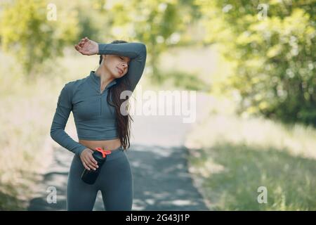 Tired runner woman jogger relaxing with bottled water after jogging in park outdoor. Stock Photo