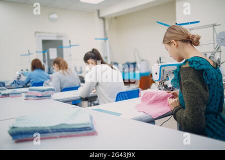 Young beautiful seamstress sews on sewing machine in factory Stock Photo