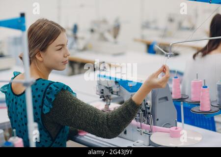 Young beautiful seamstress sews on sewing machine in factory Stock Photo