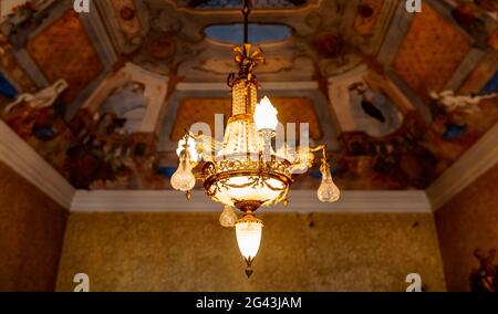Empire style golden chandelier. Antique chandelier on the ceiling with the lights on. Stock Photo