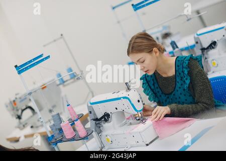 Young beautiful seamstress sews on sewing machine in factory Stock Photo