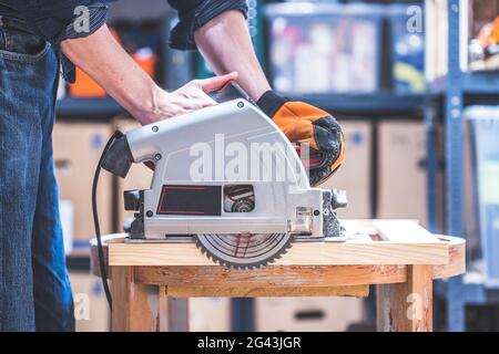 Sawing wood in the garage: Home handyman sawing plank of wood with circular saw Stock Photo