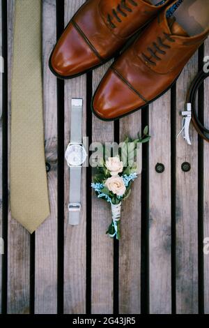 Wedding details of the groom - boutonniere, shoes, tie and watch on a wooden background, top view. Stock Photo