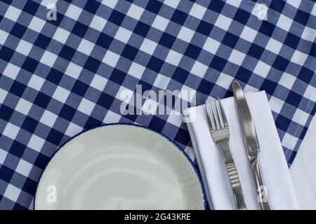 Plate, fork and knife on a served table with blue white checkered tablecloth. Catering concept. Stock Photo