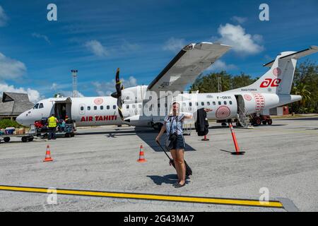 Smiling woman with camera exits Air Tahiti ATR 72-600 airplane on apron at Bora Bora Airport (BOB), Bora Bora, Leeward Islands, French Polynesia, Sout Stock Photo