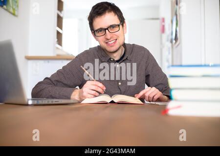 Learning and studying concept: Young happy male student is learning at home, stack of books Stock Photo
