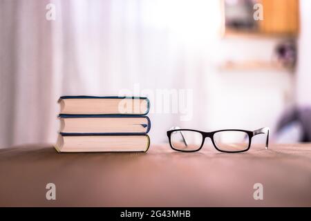 Knowledge and science concept: Stack of books and glasses lying on wooden desk, home. Stock Photo