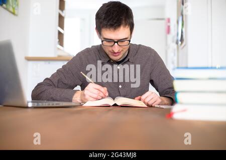 Learning and studying concept: Young happy male student is learning at home, stack of books Stock Photo