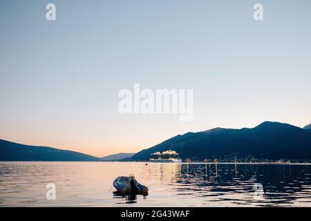 The cruise liner sails through Kotor Bay at night, against the backdrop of the mountains. Rubber motorboat in the foreground in Stock Photo