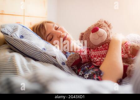 Restful sleep: Young female is sleeping in her bed, teddy bear Stock Photo