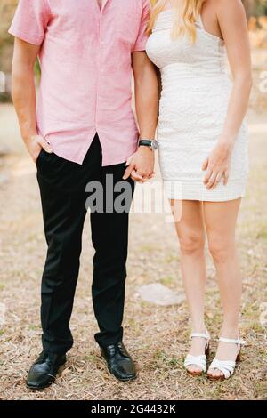 A man in a pink shirt and a woman in a short white dress stand side by side and tenderly hold a hand Stock Photo
