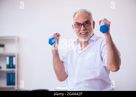 Old businessman employee doing sport exercises in the office Stock Photo