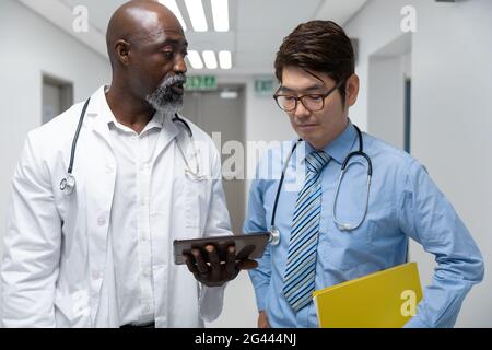Couple of diverse male doctors walking through corridor looking at tablet Stock Photo