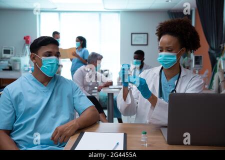 Mixed race couple of doctors wearing face masks preparing to make injection Stock Photo