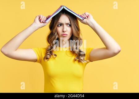 Photo of funny woman holding book over head, confused expression Stock Photo