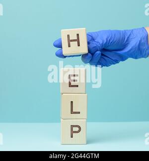 Inscription help on wooden cubes and a hand in a blue medical glove. First aid concept Stock Photo