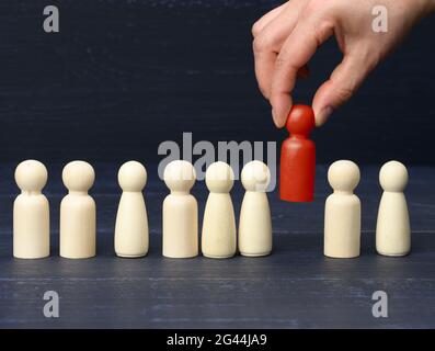 A female hand holds a wooden red figurine chosen from the crowd. The concept of finding talented employees Stock Photo