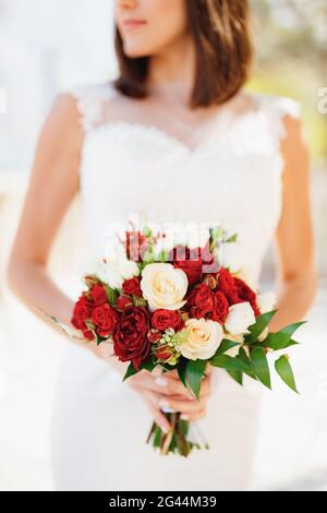Bride in a beautiful white dress holds a bouquet of red and pink roses in her hands Stock Photo