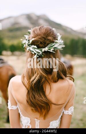 Bride is standing with her back in a beautiful lace dress. Bride's head is adorned with a wreath of green olive branches Stock Photo