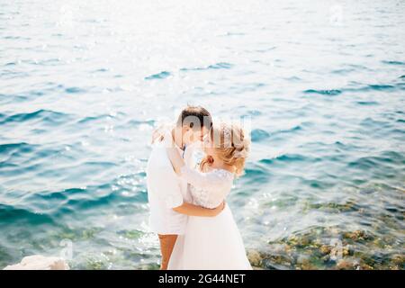 The bride and groom are embracing on the rocky seashore and are about to kiss Stock Photo