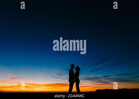 Silhouettes of a couple holding hands against the background of the sunset in the mountains Stock Photo