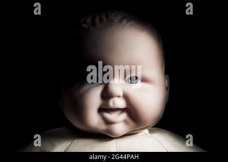 Creepy doll face. It seems like character of horror movie. Angry baby doll, fear of living ghost. Halloween concept. Low-key lig Stock Photo