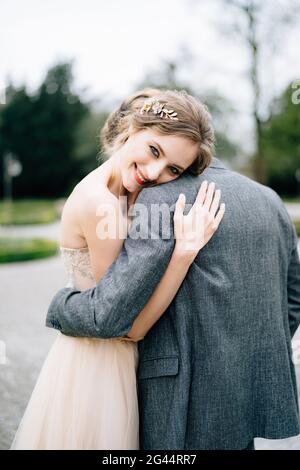 Smiling bride rested her head on the shoulder of the groom hugging her in the park. Lake Como, Italy Stock Photo