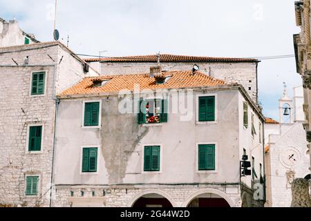 Old three-story residential building with green shutters and orange tiles on the roof. Stock Photo