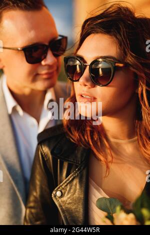 Portrait of bride in sunglasses and a black leather jacket on the background of groom Stock Photo