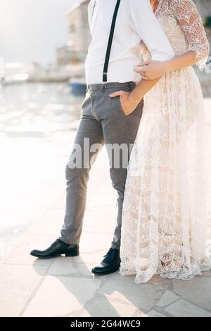 Bride hugs groom from behind while standing on the pier against the background of the port. Bottom view Stock Photo