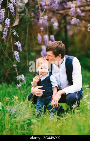 Father is kissing his baby boy on top of the head with a wysteria blooming in the background Stock Photo