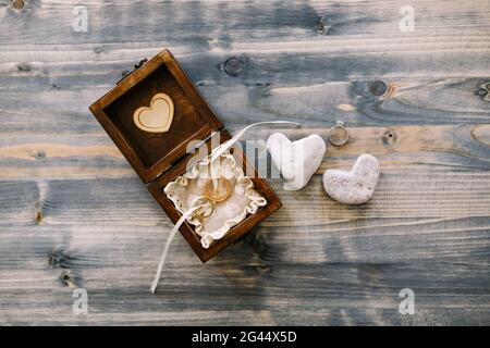 An open wooden box with wedding rings and two heart-shaped pebbles on a gray wood background. Stock Photo
